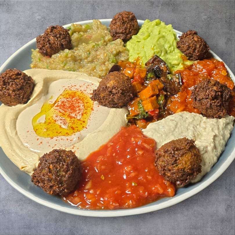 A platter of falafel, hummus, baba ghanoush, guacamole, and various vegetable dips.