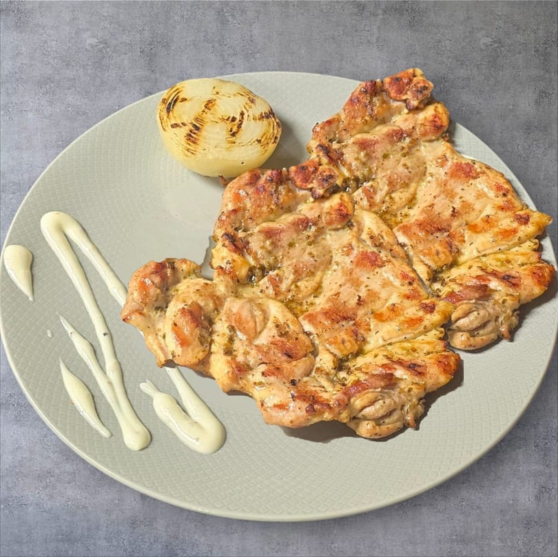 Grilled chicken thighs with a side of grilled onion and white sauce on a light green plate.