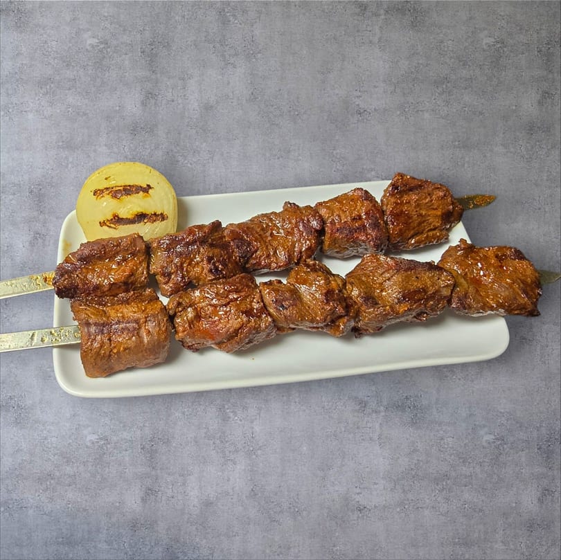 Two skewers of grilled beef cubes and a grilled onion half on a white rectangular plate.