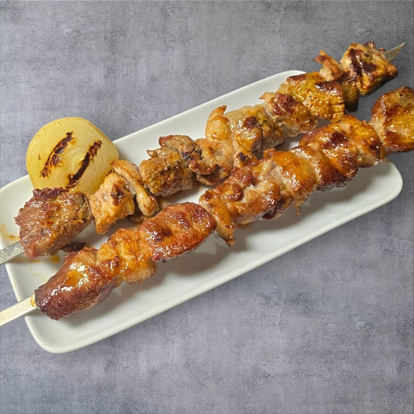 Two skewers of grilled meat and a grilled onion half on a white rectangular plate.